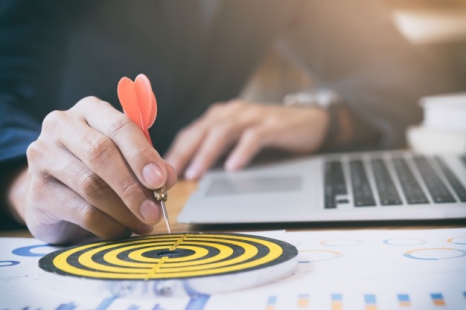 
	Businessman aims at bullseye with a dot while sitting with a computer 

